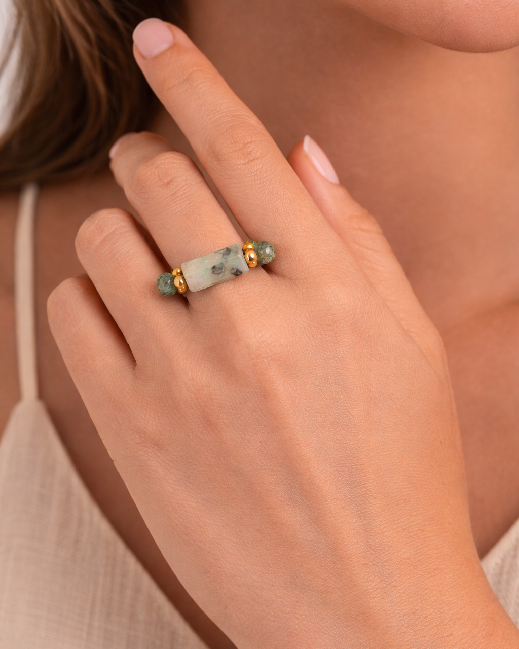 Close-up of a hand wearing a ring with a natural stone on a neutral background