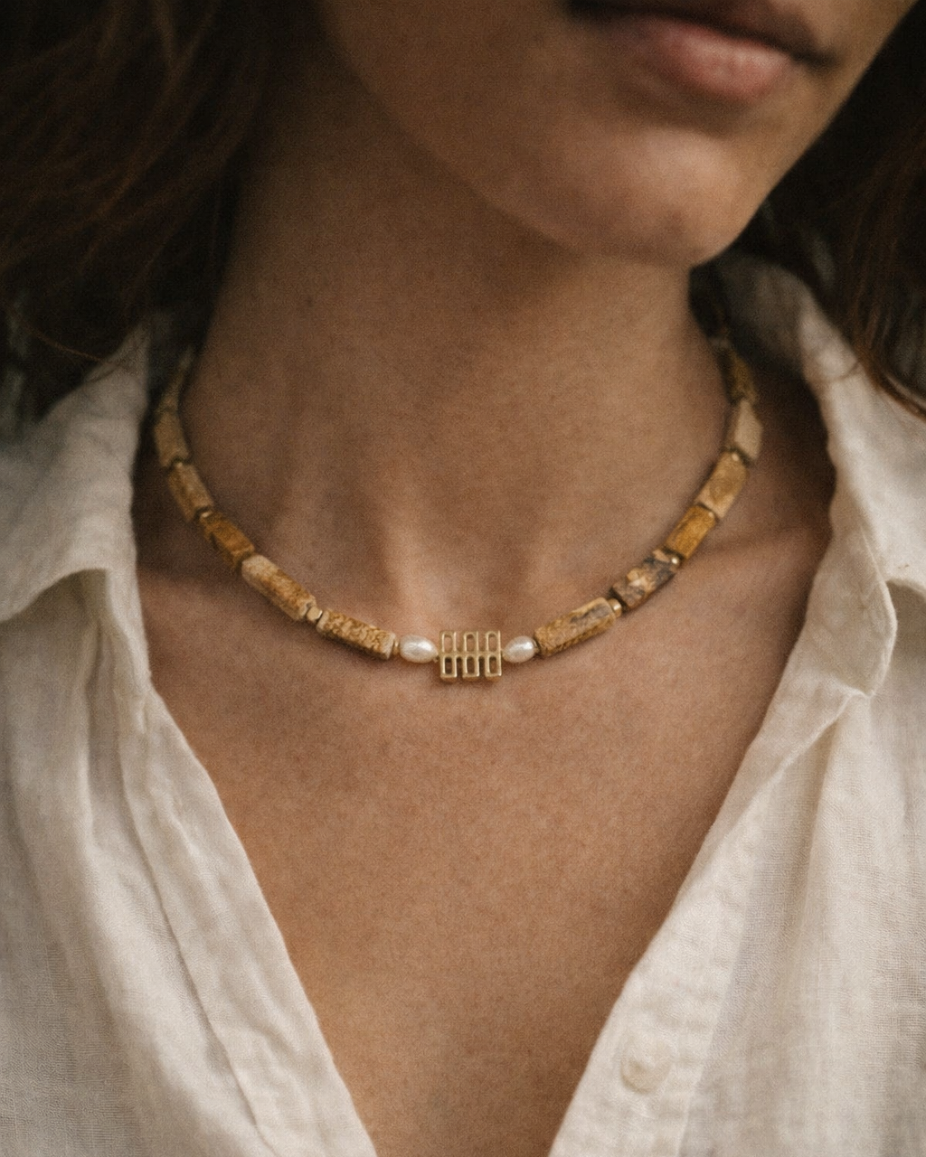 Close-up of a person wearing a gold necklace with a white shirt.