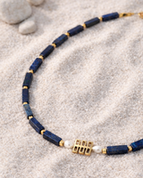 Necklace with blue beads and gold accents on a sandy surface